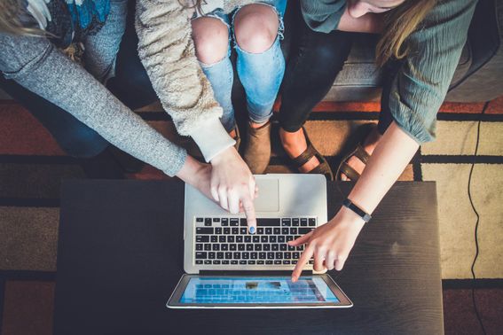 a group of three young people looking at a laptop together to select items online