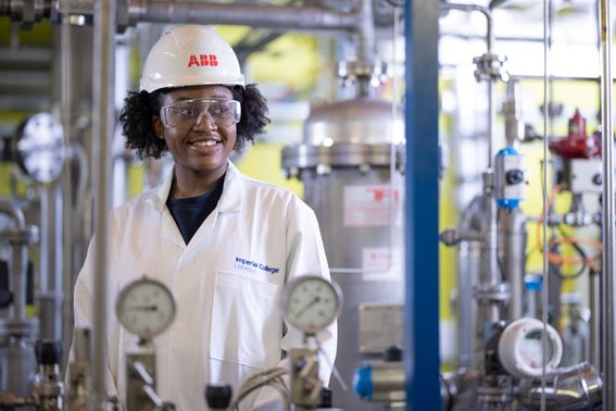 Undergraduate student in engineering lab sitting on workspace with clamps and equipment behind