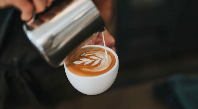 Person pouring milk into a coffee cup