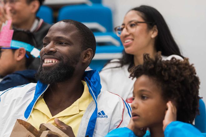 A man and a child in a lecture theatre look towards the presenter while smiling