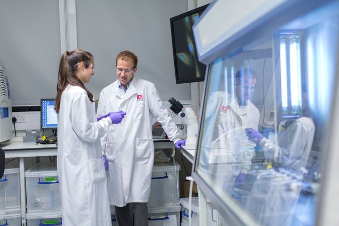 Two researcher in lab coats discuss a sample in a lab