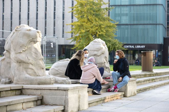 Students sit by the lion statues at the base of the Queen's Tower on Dangoor Plaza at South Kensington Campus