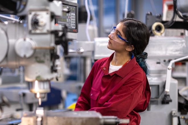 A woman wearing protective clothing uses a machine in the Mech Eng workshop