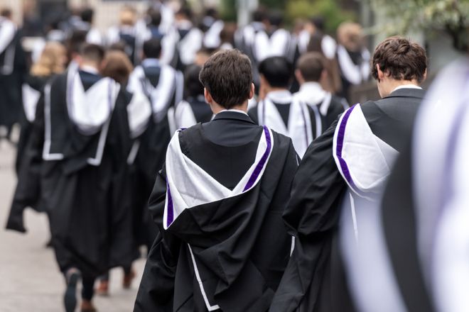 The backs of graduates as they walk on campus in their gowns