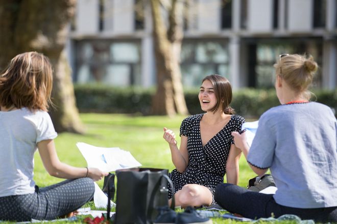 Three women laugh as they sit on the grass in Prince's Gardens