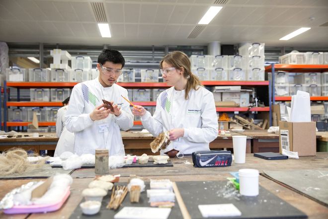 Two design engineering students examine different materials laid out on a bench in a workshop