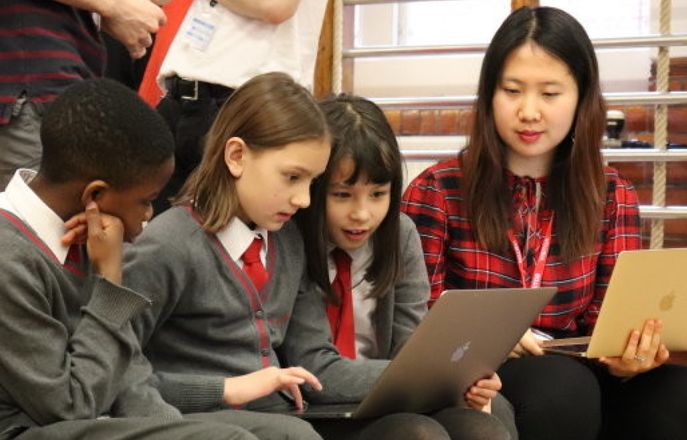 School children and Imperial Computing student gathered around laptops