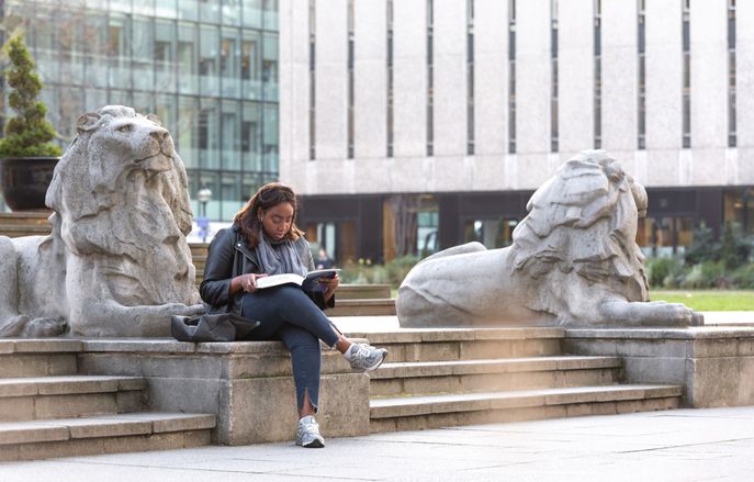 An MBBS student reading near Queen's Lawn on Imperial's South Kensington Campus