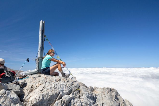 A student sitting on top of a mountain looking out over clouds
