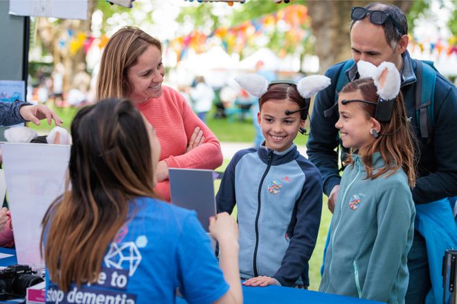 Two young girls wearing rabbit headsets smile at UK DRI stall at the festival