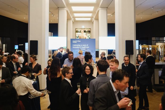 People standing at an evening reception, in front of IGHI sign