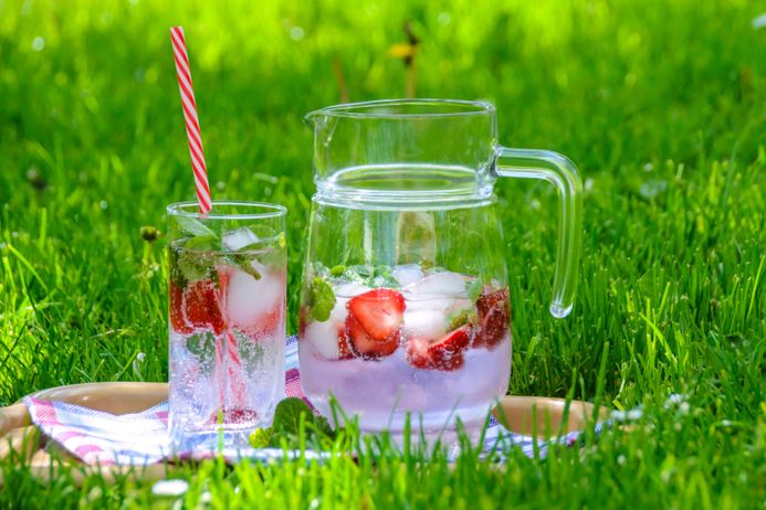 A glass and jug filled with a drink made with fresh strawberries on a field of grass