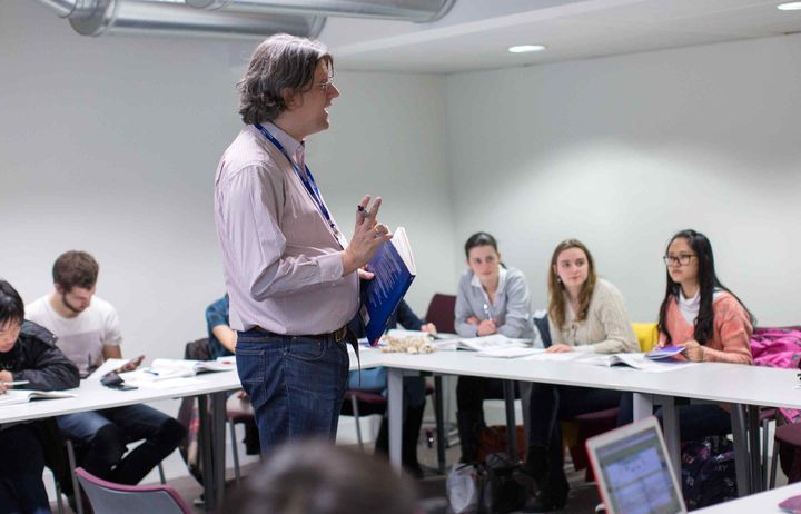 Lecturer speaking and teaching a small seminar of students sitting at tables in a horseshoe