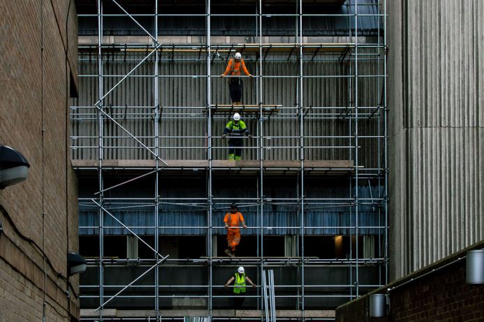 Construction workers on different levels of scaffolding in front of a building