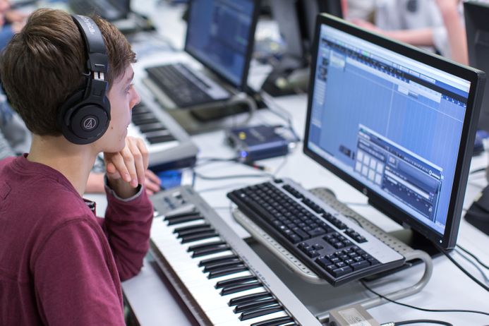 student with headphones producing music with keyboard and computer