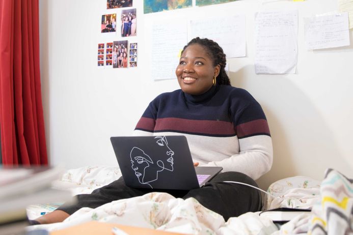 Undergraduate student sitting in bed with laptop in halls