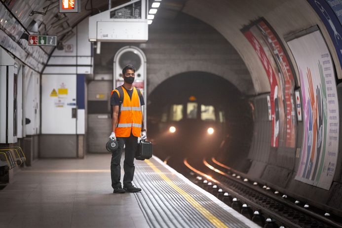 A researcher holding environmental sampling devices stands on a platform of the London Underground as a tube train approaches through a tunnel