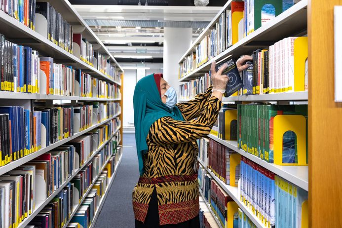 A librarian wearing a facemask replaces a book on a shelf in the Central Library