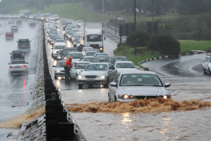 A flooded road with a long traffic jam and one car attempting to drive through it with water up to the headlights