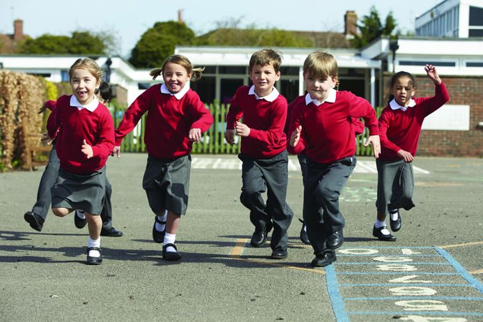 A group of children in school uniform running on a playground