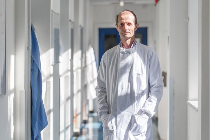 Professor Robin Shattock wearing a white coat, walking down a corridor