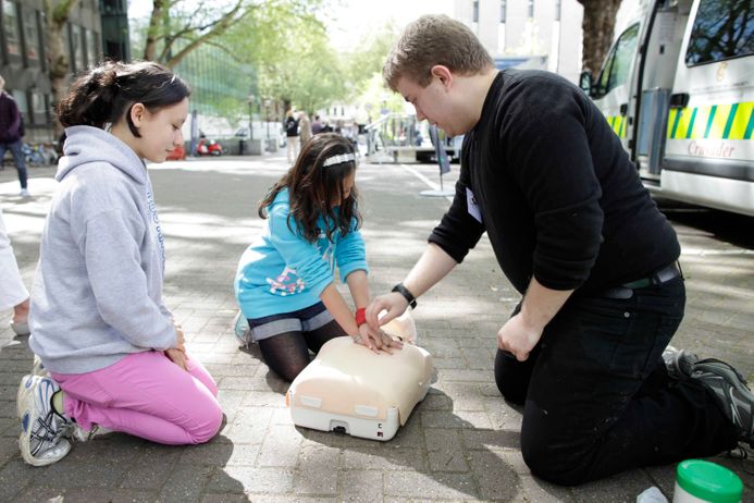 man teaching two girls to do CPR on a manikin
