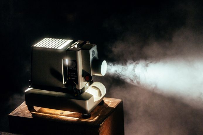 A movie projector with light shining out from it against a dark background