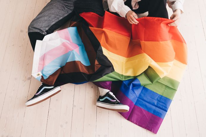 Two people sitting under a LGBTQ progress pride flag