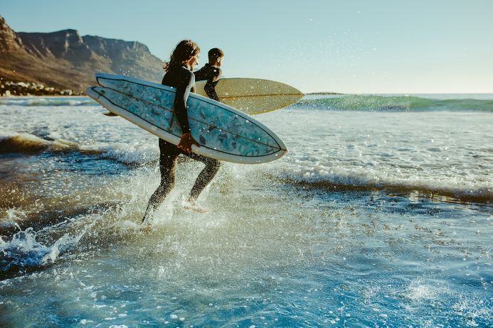 Two men carrying surfboards running in to the sea for surfing.