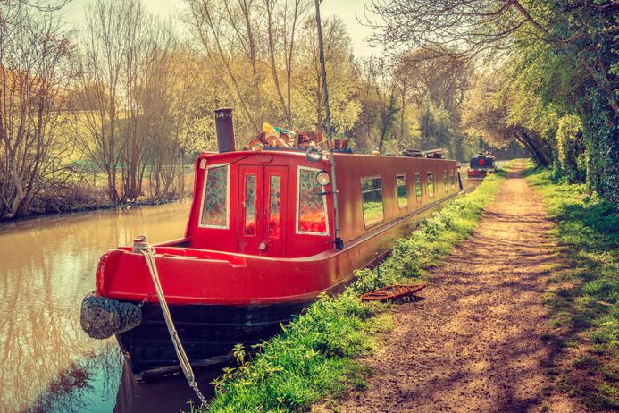 Red narrow canal boat in countryside waterway