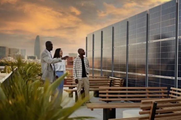 Three people standing in an open air space with benches, looking at a wall of solar panels