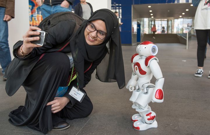 A young woman stoops down to take a photo with a humanoid robot.
