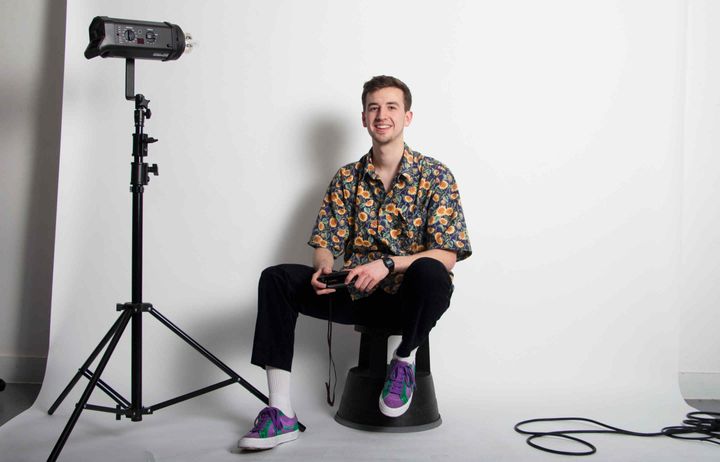 PhotoSoc member Aidan Cunnington sat on a stool holding a camera