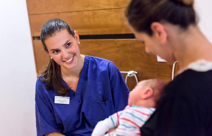 A nurse smiling at a new mother and her baby