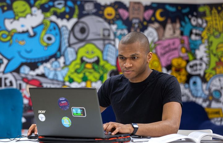 A man working at a laptop in front of a colourful mural