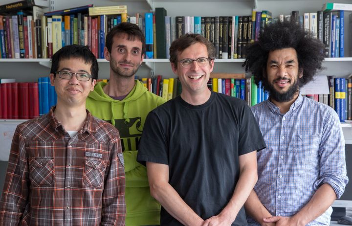 A mathematics professor with some of his students in his office on the South Kensington campus at Imperial. They're photographed smiling in front of shelve full of books