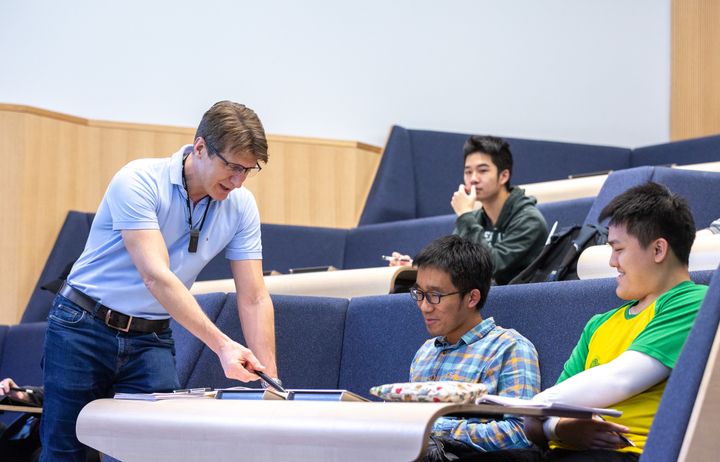Lecturer showing two male students how to solve a problem