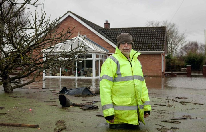 A man in high viz standing thigh deep in floodwater outside a house with a conservatory