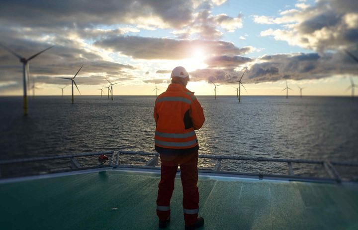 Man on a platform at sea looking out at offshore wind turbines