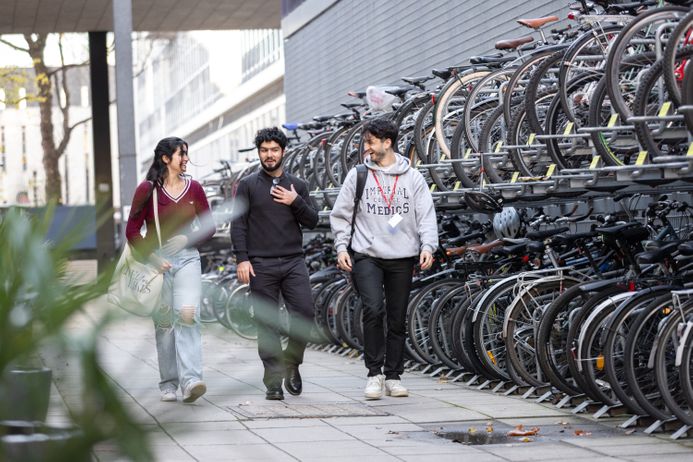 Three students walking past a bike shed