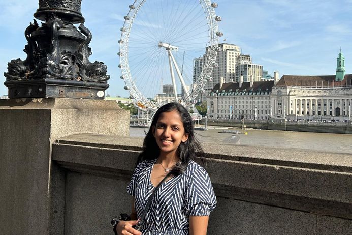 A smiling student standing by the River Thames with the London Eye in the background