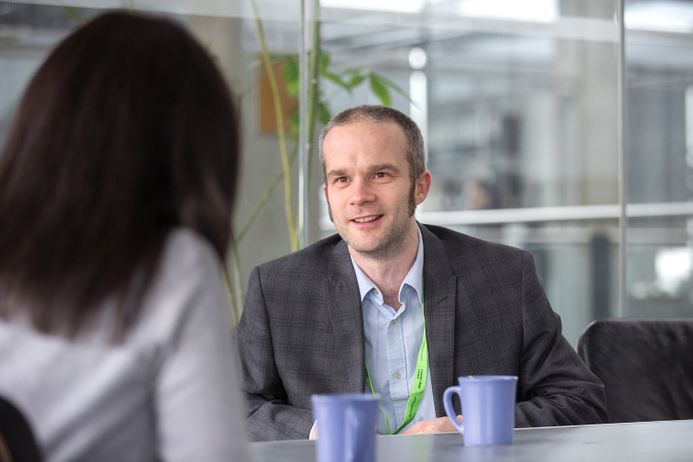 A man wearing a Mental Health First Aid green lanyard in conversation with a member of staff