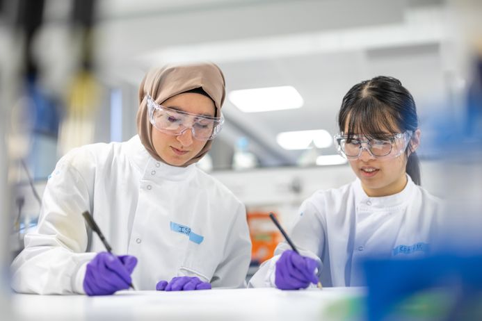 Photo capturing two female medicine scholars in the laboratory environment writing notes