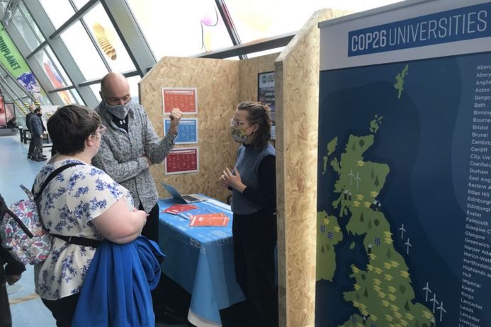 Two members of the public talking to someone behind a stand in an exhibition space at the climate summit