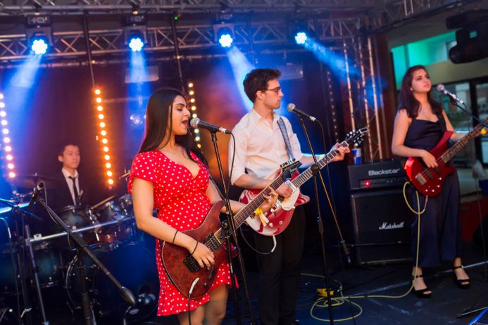 Band playing on stage female singer playing guitar with drummer and other guitarists