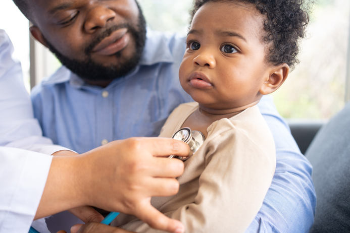 Baby in father's lap being checked by doctor