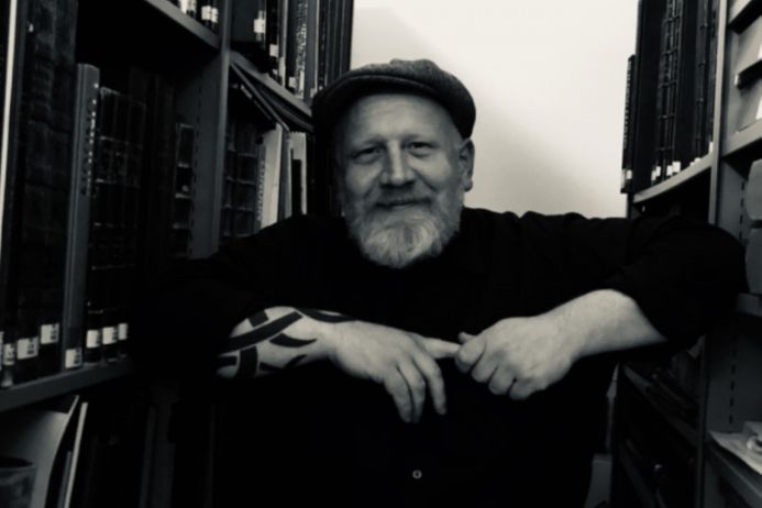 black and white photo of Stef Dickers in archive with shelves on either side