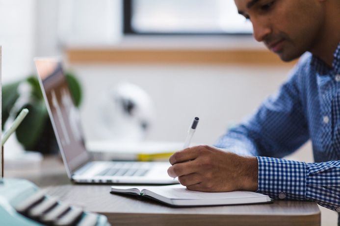 Man writing in a notebook next to a laptop