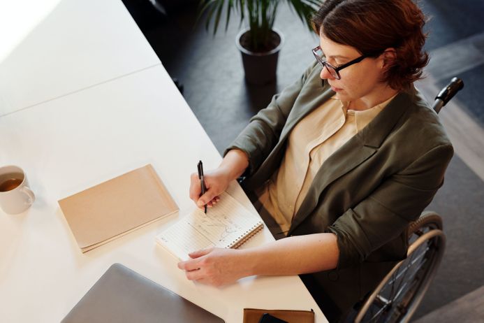 A person in a wheelchair writing notes at a desk