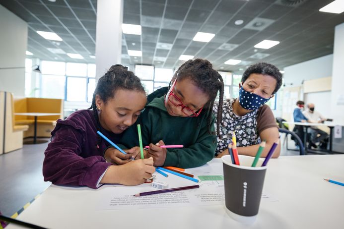 Two children colouring with an adult in the background